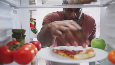 vista mirando desde el interior del refrigerador mientras el hombre abre la puerta para las sobras de una rebanada de pizza para llevar