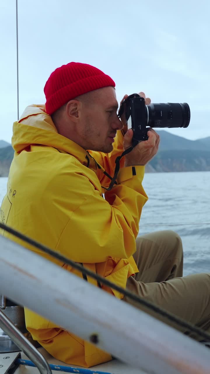 Man in Yellow Raincoat Taking Photos on a Sailing Boat