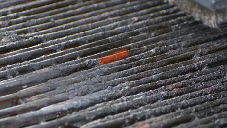 A-wire-brush-cleans-a-grill-as-a-small-flame-burns-on-some-old-food