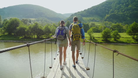 Ein-Paar-Touristen-Gehen-Vorsichtig-über-Eine-Brücke-über-Einen-Bergfluss-4k-Video