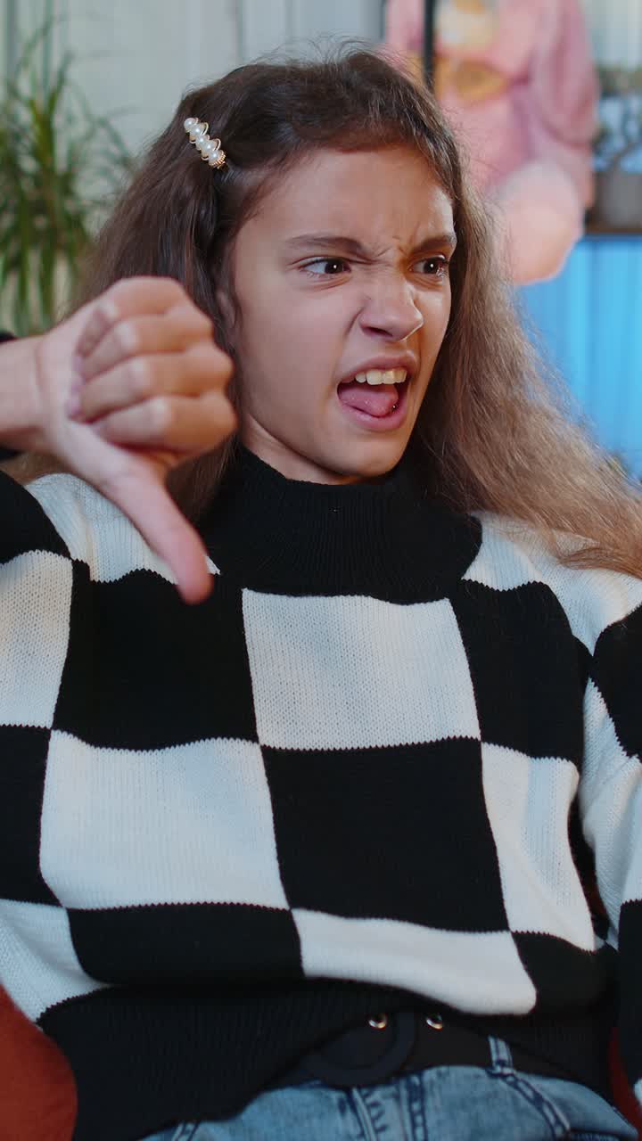 Upset young girl showing thumbs down dislike bad work disapproval dissatisfied feedback at home