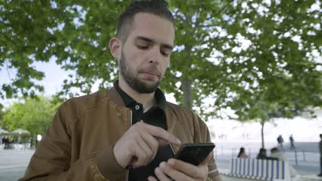 un joven pensativo caminando por el parque con un teléfono inteligente.