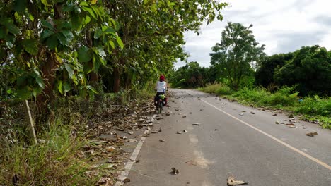 A-solo-Asian-woman-long-distance-cyclist-and-backpacker-dressed-in-athletic-clothes-riding-through-Nan-province-on-her-foldable-bicycle-on-the-left-corner-of-the-road,-Thailand