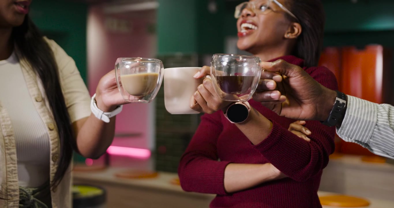 Coworkers reacting to central woman's comment, raising mugs in office kitchen toasting together