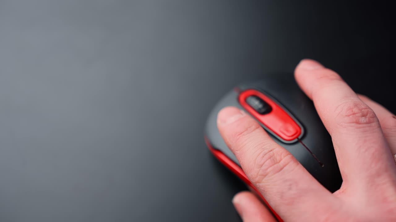 Close-up of a hand moving a black and red wireless mouse on a clean dark desk with copy space, showing office productivity and computer navigation in a minimal workspace
