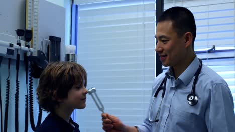 Seitenansicht-Eines-Jungen-Asiatischen-Arztes,-Der-Einem-Kaukasischen-Patienten-In-Der-Klinik-Die-Stimmgabel-Zeigt-4k