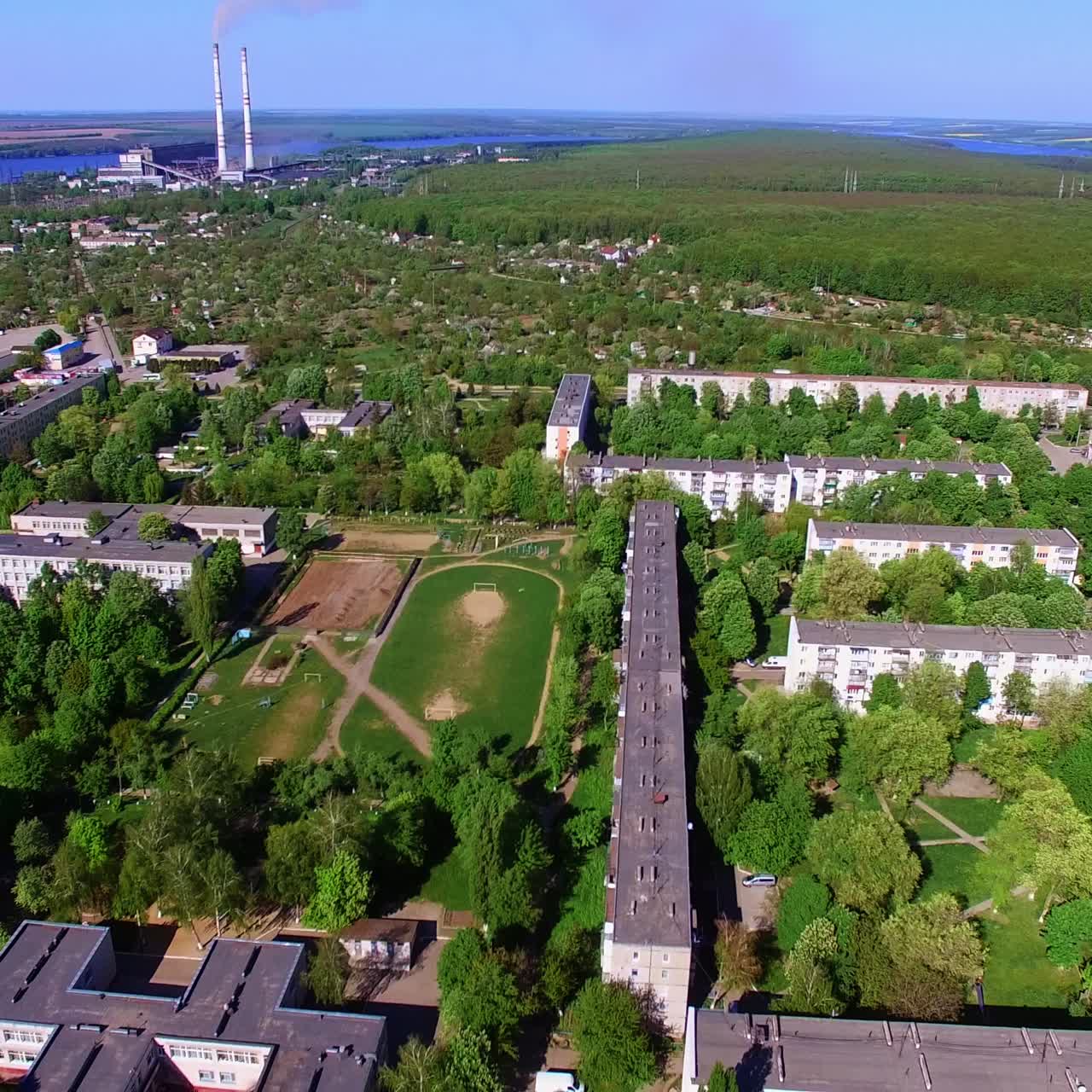 Big green city panorama on summer day. Drone footage over the residential area at the backdrop of blue river, farmlands and woods