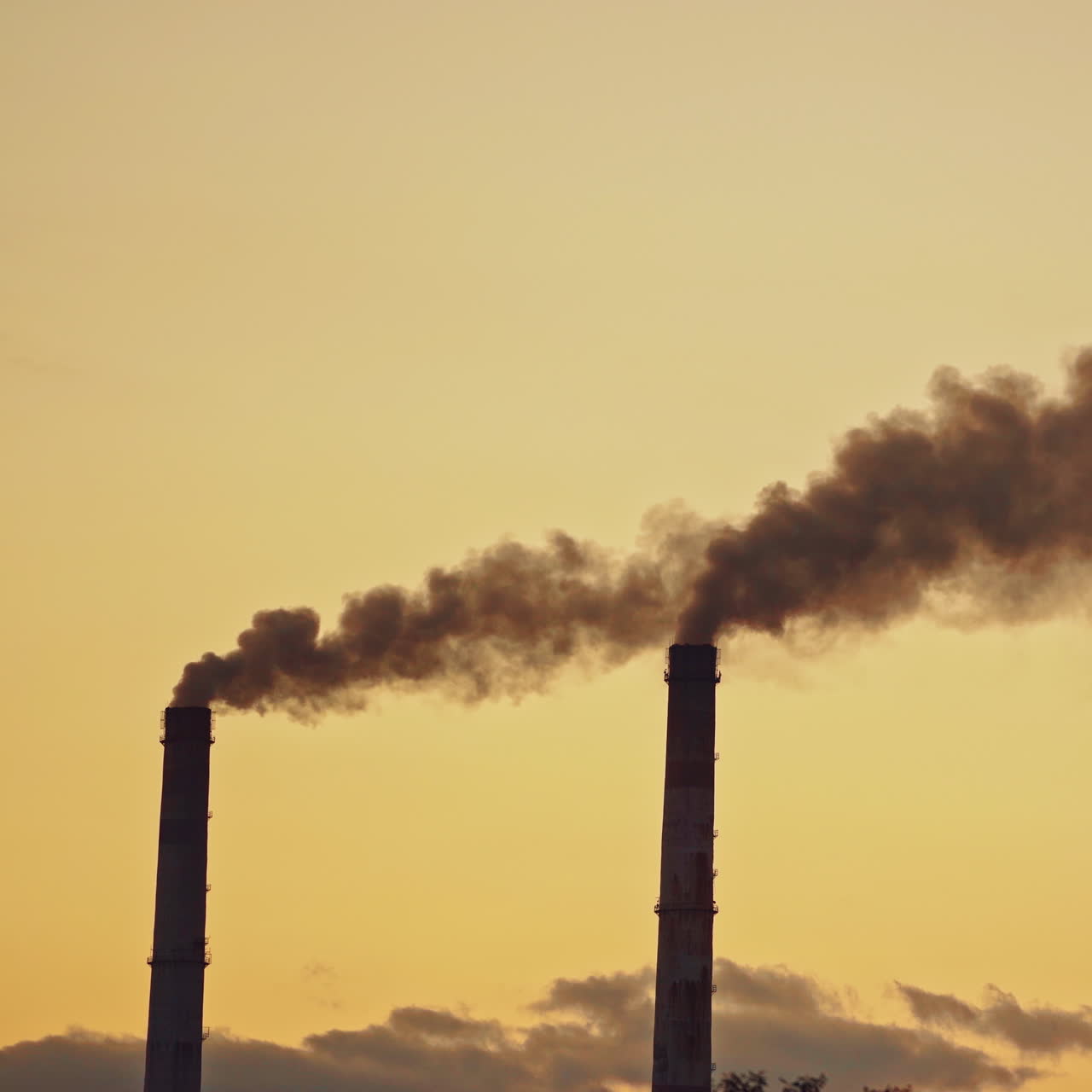 Dark smoke comes from large pipes into the air on the evening sky background. Dirty emissions pollute the environment. Ecological problems in the air.