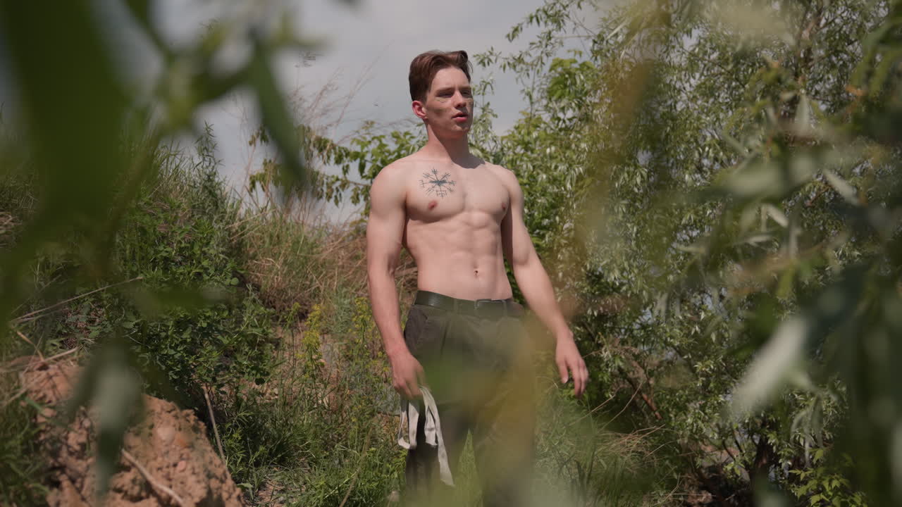 warrior loosening headband and gently parting hair with eyes closed in relief amid riverside grasses beneath cloudy sky after intense survival training conveying calm determination and mindful focus
