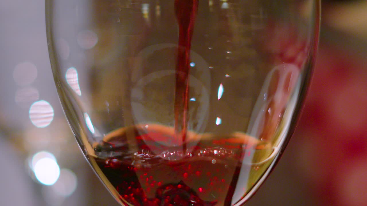 Red Wine Being Slowly Poured into a Glass in Slow Motion with Shallow DOF. Alcoholic Drink Served at Bars and Restaurants