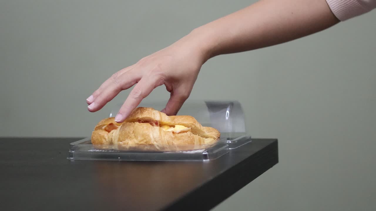 persona abre el recipiente, lo saca y come un croissant