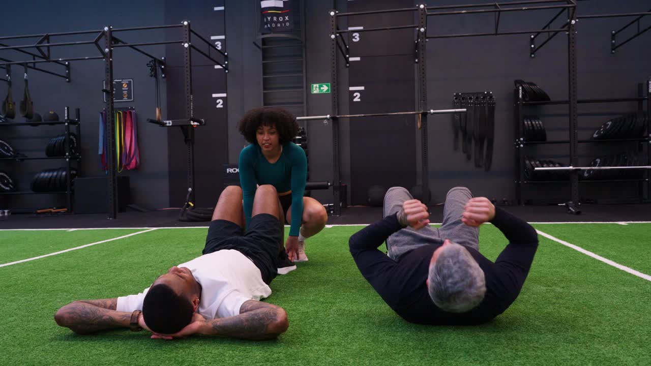 Two Men Doing Sit-Ups with a Female Coach in a Modern Gym