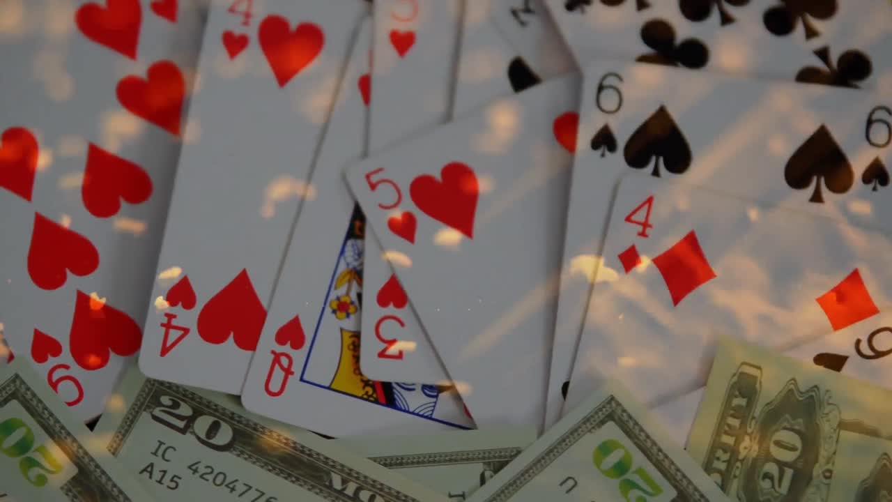 Animation of gold confetti falling over playing cards and dollar bills on gambling table