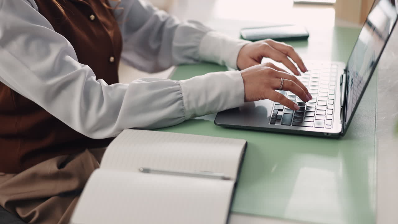 Woman writing in notebook at desk with laptop