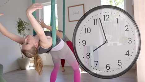 animación de un reloj que se mueve rápidamente sobre una instructora caucásica y una adolescente haciendo yoga aéreo