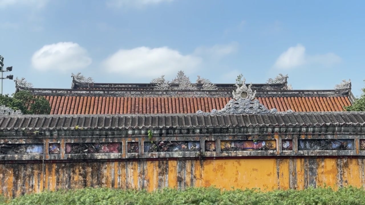 Dinding kuning berukir dengan atap genteng tradisional dan motif kekaisaran dekoratif di Kota Kekaisaran Hue. Arsitektur Vietnam bersejarah yang menampilkan warisan budaya, keahlian, dan sejarah