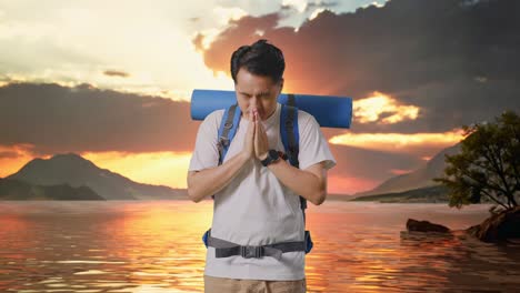 excursionista masculino asiático con mochila de montañismo rezar por algo en un lago