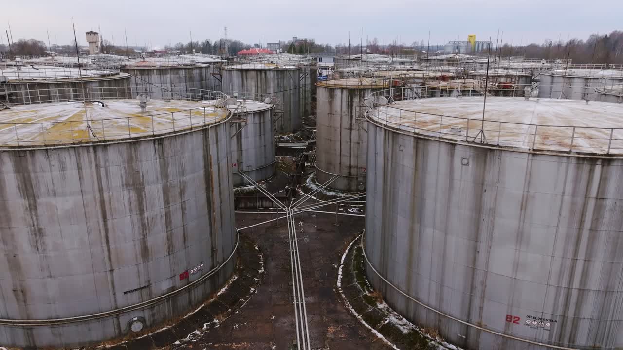Drone flying through an old fuel storage site, rusted metal tanks and pipelines