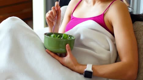 Woman-having-breakfast-on-sofa-in-living-room