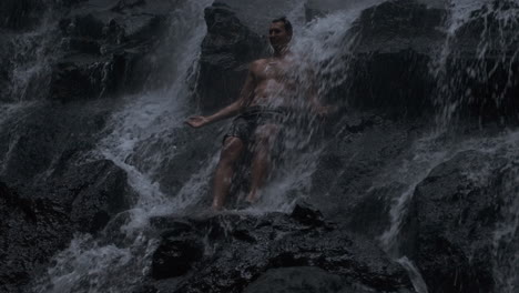 young man standing under waterfall.