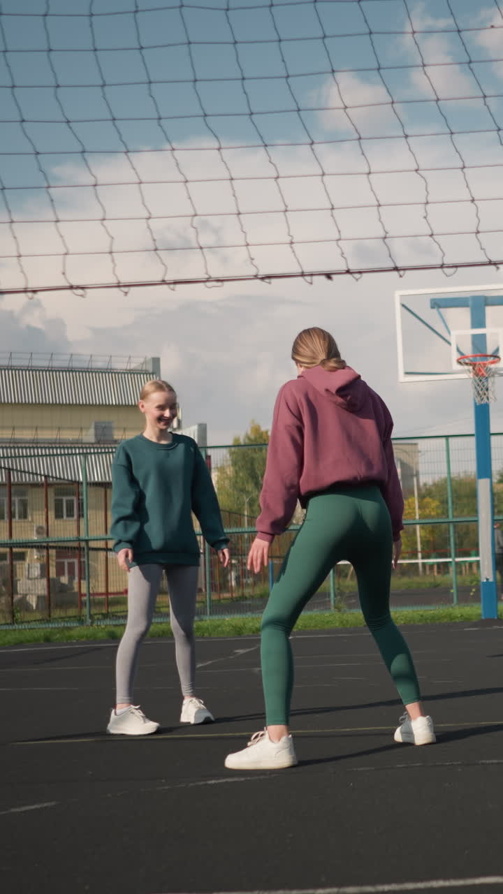 tres jugadores de voleibol en la cancha se pierden la pelota servida a ellos, dos damas posan lúdicamente mientras otras miran, atmósfera animada en la arena deportiva con vegetación y edificio en el fondo
