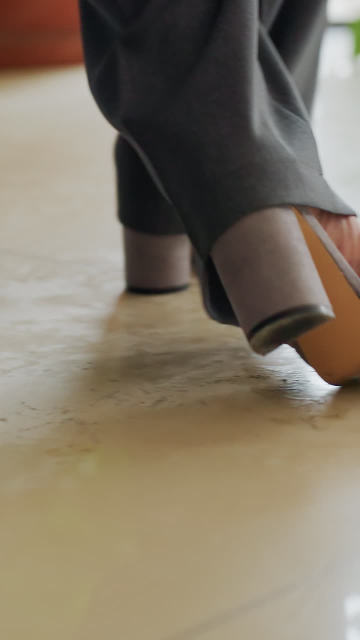 Close-up of businesswoman's feet in gray heels walking confidently across polished office floor, emphasizing motion, elegance, and professionalism in corporate setting