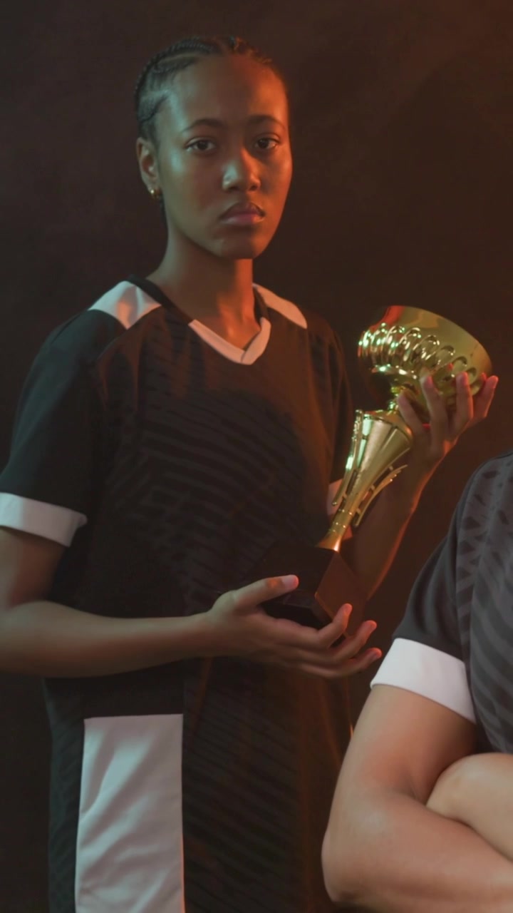 Video verticale: La telecamera zooma su un calciatore in maglia nera che culla un trofeo d'oro mentre posa in studio.