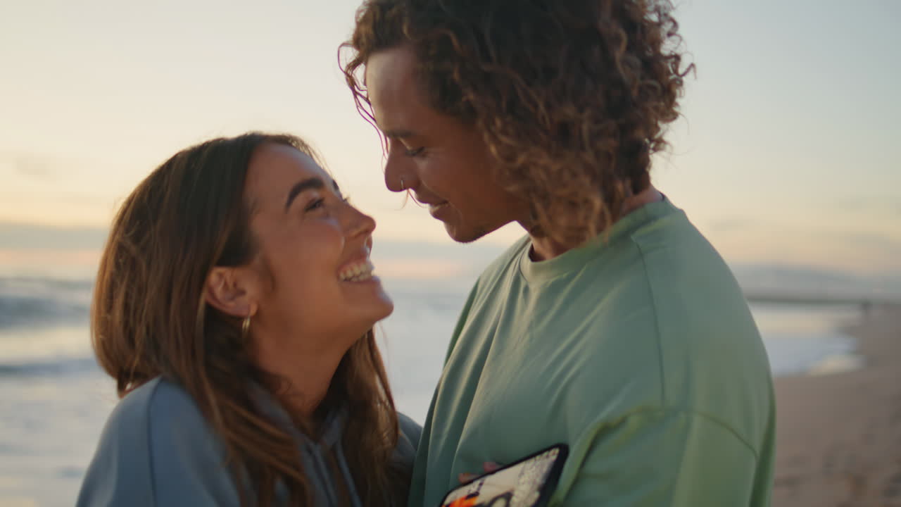 Love pair looking smartphone sunrise sea closeup. Young man kissing girlfriend