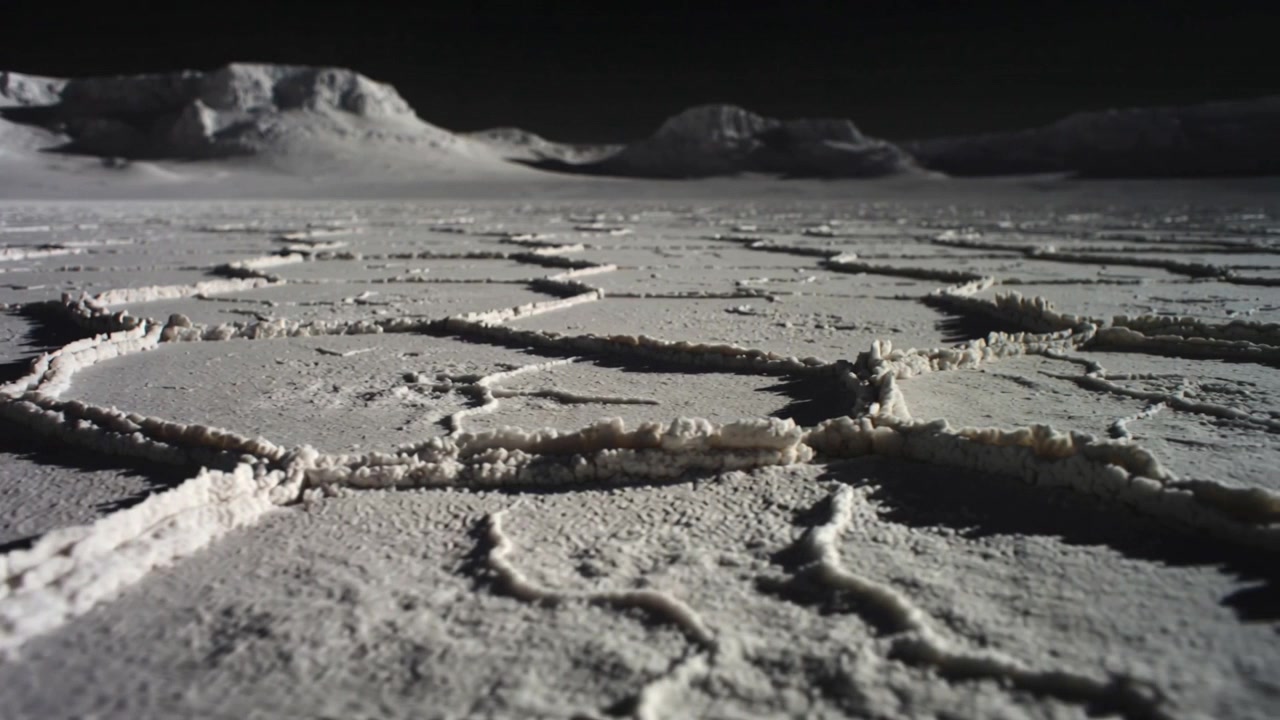 Pulling back low-angle camera showing cracked plates toward distant mesas with raised circular rims