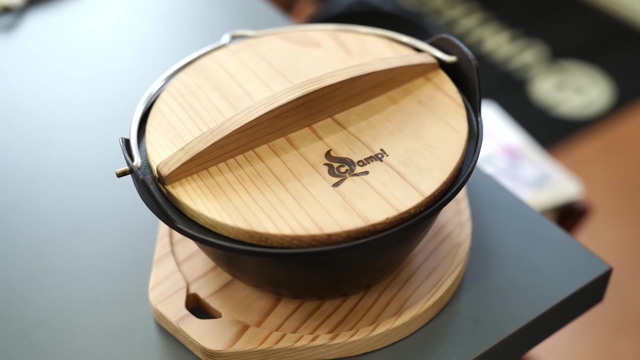 Mani che aprono il coperchio di legno di una pentola in ghisa finita su un supporto di legno
