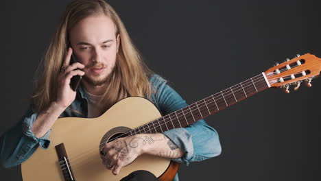 Un-Joven-Caucásico-Con-Guitarra-Teniendo-Una-Llamada-En-Un-Teléfono-Inteligente.