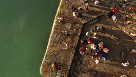 Forty-Foot,-Christmas-Swim,-Sandycove,-Ireland,-Drone-Bird's-Eye-View-Orbit-Pulling-Back-as-Swimmers-Jump-into-Sea