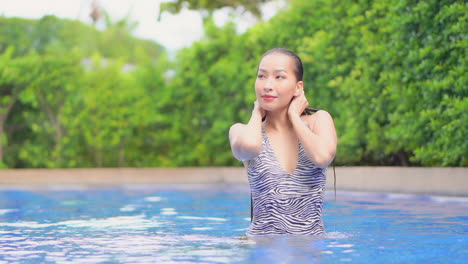 Beautiful-Brunette-Asian-Woman-Squeezing-Water-from-Wet-Hair-While-Bathing-in-a-Swimming-Pool-Touching-Head-with-Closed-Eyes---face-close-up-slow-motion