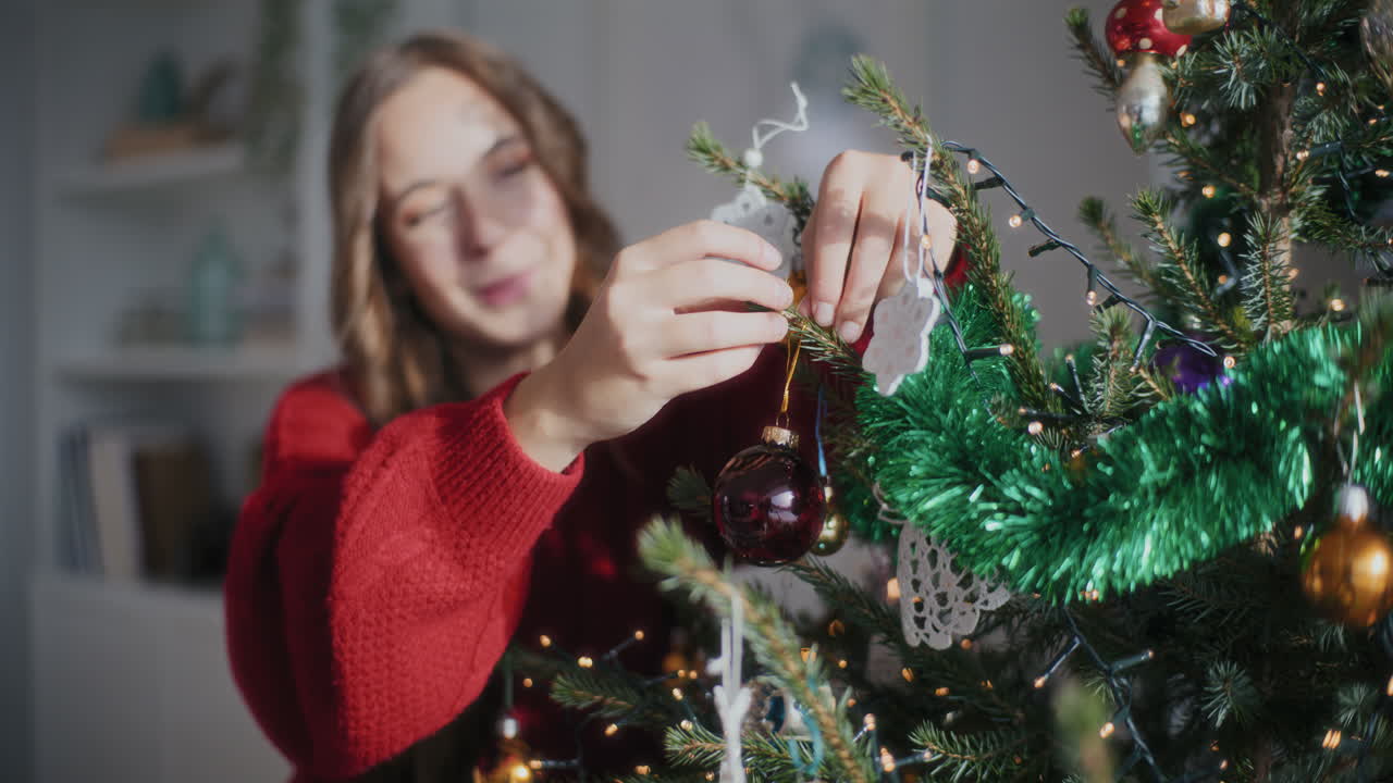mujer alegre colgando adornos en el árbol de navidad en casa