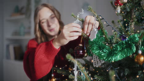 cheerful woman hanging bauble on christmas tree at home