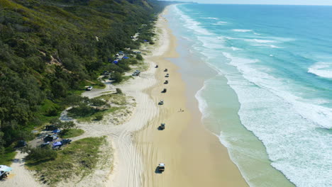 Drone-Aéreo-De-4k-Sobre-Autos-4wd-Conduciendo-En-Una-Playa-De-Arena-Con-Olas-Azules-Del-Océano-Lamiendo-La-Costa-En-Australia