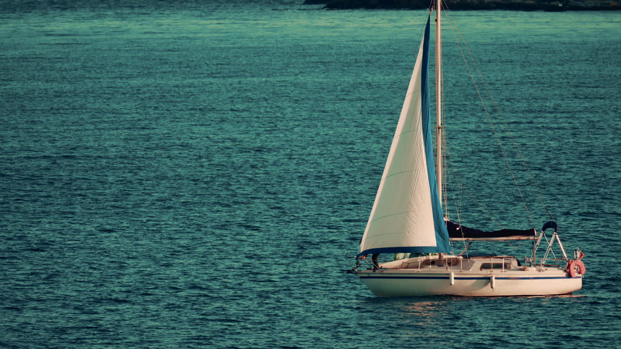 Sailboat with blue and white sails gliding across calm open water on a sunny afternoon