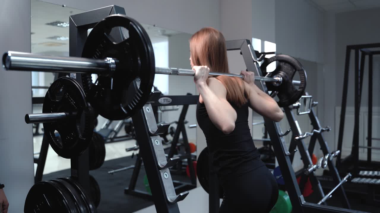 Slender woman in sportswear comes to the weight bar and lifts it in the gym near the mirror. Healthy lifestyle