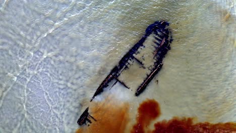 vista aérea de un naufragio en una playa con agua turquesa, metal de color óxido en el barco y arena blanca que rodea el naufragio