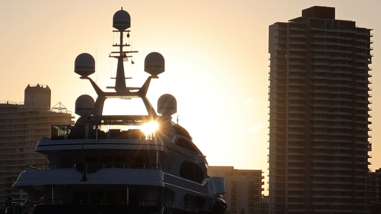 La silhouette di uno yacht incorniciata da un tramonto luminoso e grattacieli urbani.