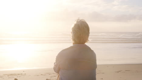 Vista-Trasera-De-Una-Mujer-Mayor-En-La-Playa-Viendo-La-Puesta-De-Sol-Sobre-El-Océano