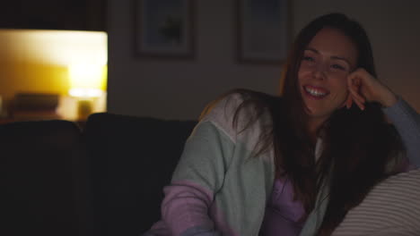 Smiling-Woman-Sitting-On-Sofa-At-Home-At-Night-Streaming-Or-Watching-Movie-Or-Show-On-Laptop-Or-TV