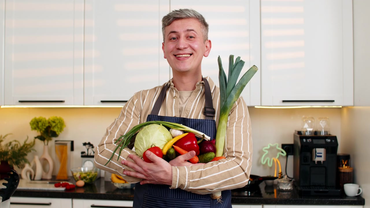 Mann mittleren Alters hält frisches Gemüse und lächelt für Diät-Ernährung und gesunde Mahlzeit in der Küche