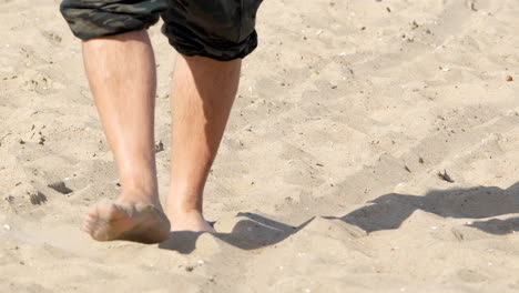 close-up of a person walking barefoot on a sandy beach, with a focus on the feet and sand