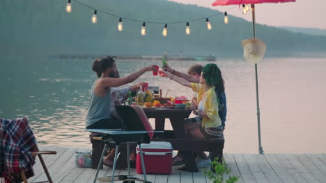 people clinking glasses at outdoor dinner party on lake pier