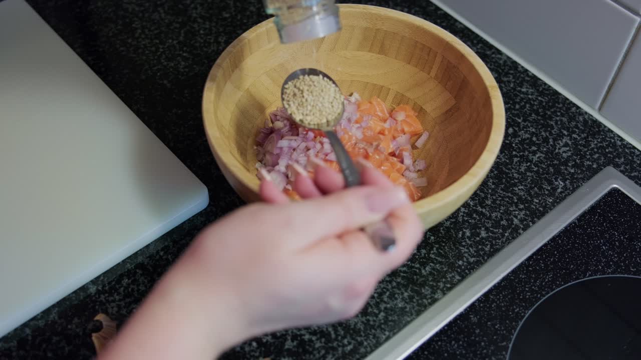 Woman's hands putting sesame seeds in a wooden bowl, interior