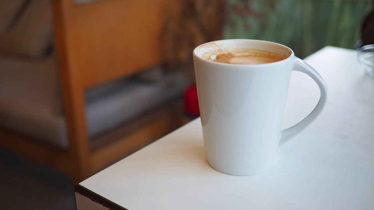 Mano che prende una tazza da caffè bianca dal tavolo.