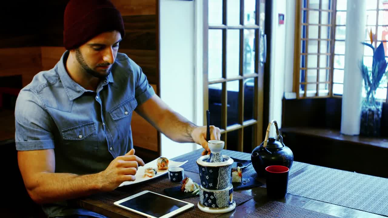 Uomo che usa un tablet digitale mentre mangia sushi