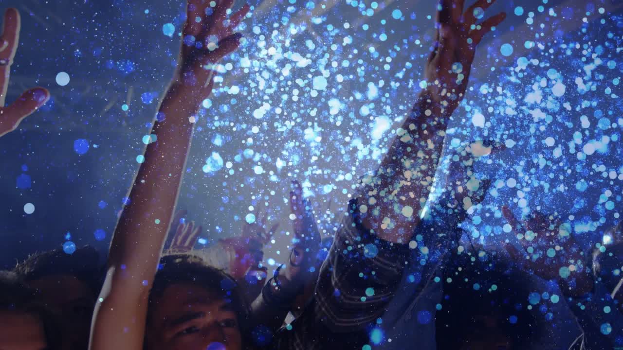 Folla che avanza, alzando le mani e acclamando al concerto, con particelle blu che avvolgono i volti.