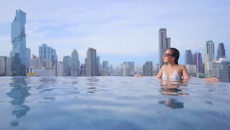 Atractiva-Mujer-Asiática-En-Una-Piscina-Infinita-Con-Impresionantes-Vistas-De-Bangkok,-El-Paisaje-Urbano-De-Tailandia,-Vacaciones-De-Lujo-Y-Concepto-De-Moda